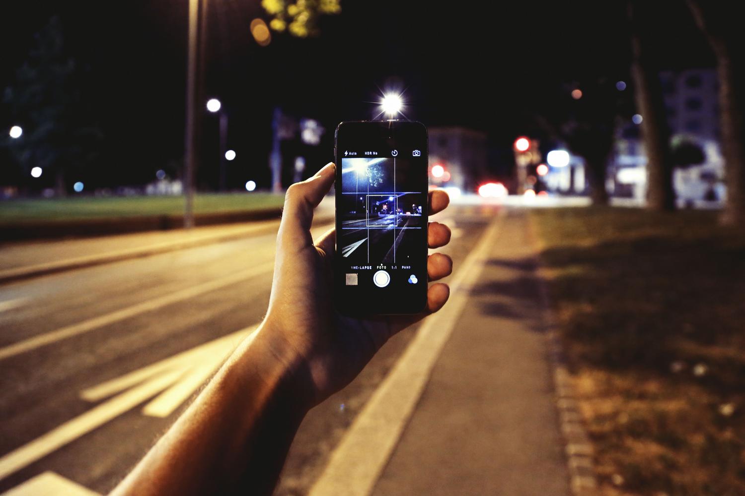 Persona, kas izmanto ielu apgaismojuma apgaismojumu Persona, kas izmanto ielu apgaismojuma apkārtējo gaismu, lai radītu kontrastu un izvairītos no trokšņa nakts fotoattēlā ar mobilo tālruni.