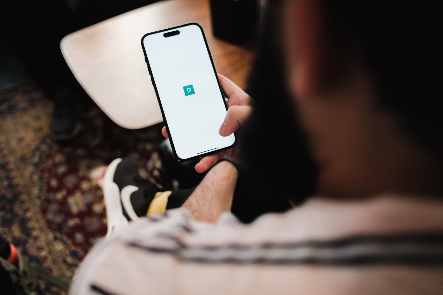 Vīrietis savā iPhone ekrānā izmanto profesionālas pārvaldības lietojumprogrammu. Vīrietis savā iPhone ekrānā izmanto profesionālas pārvaldības lietojumprogrammu.
