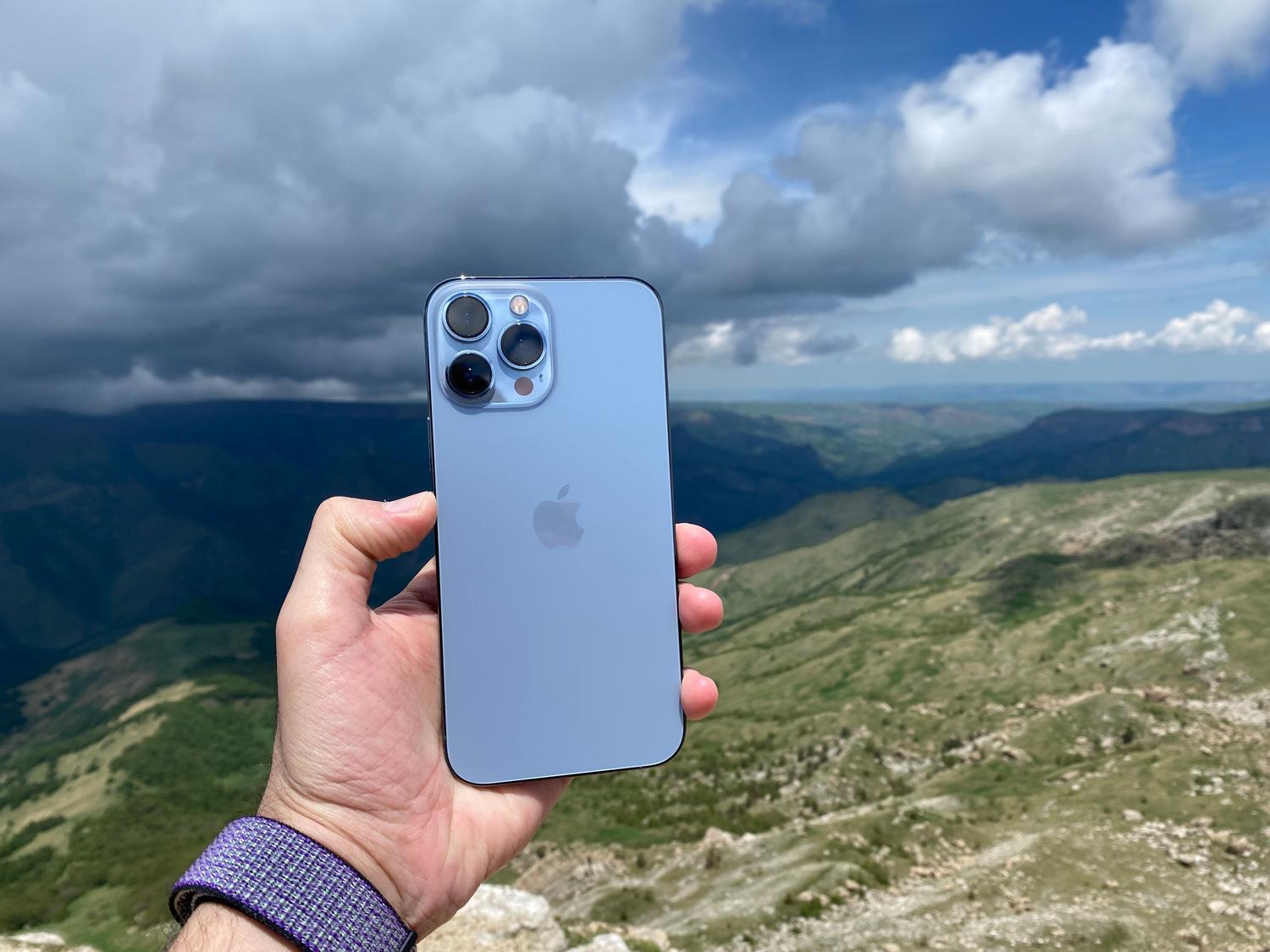 Tuvplāns ar roku, kurā tiek turēts iPhone, fonā ir satriecoša zaļu kalnu ainava