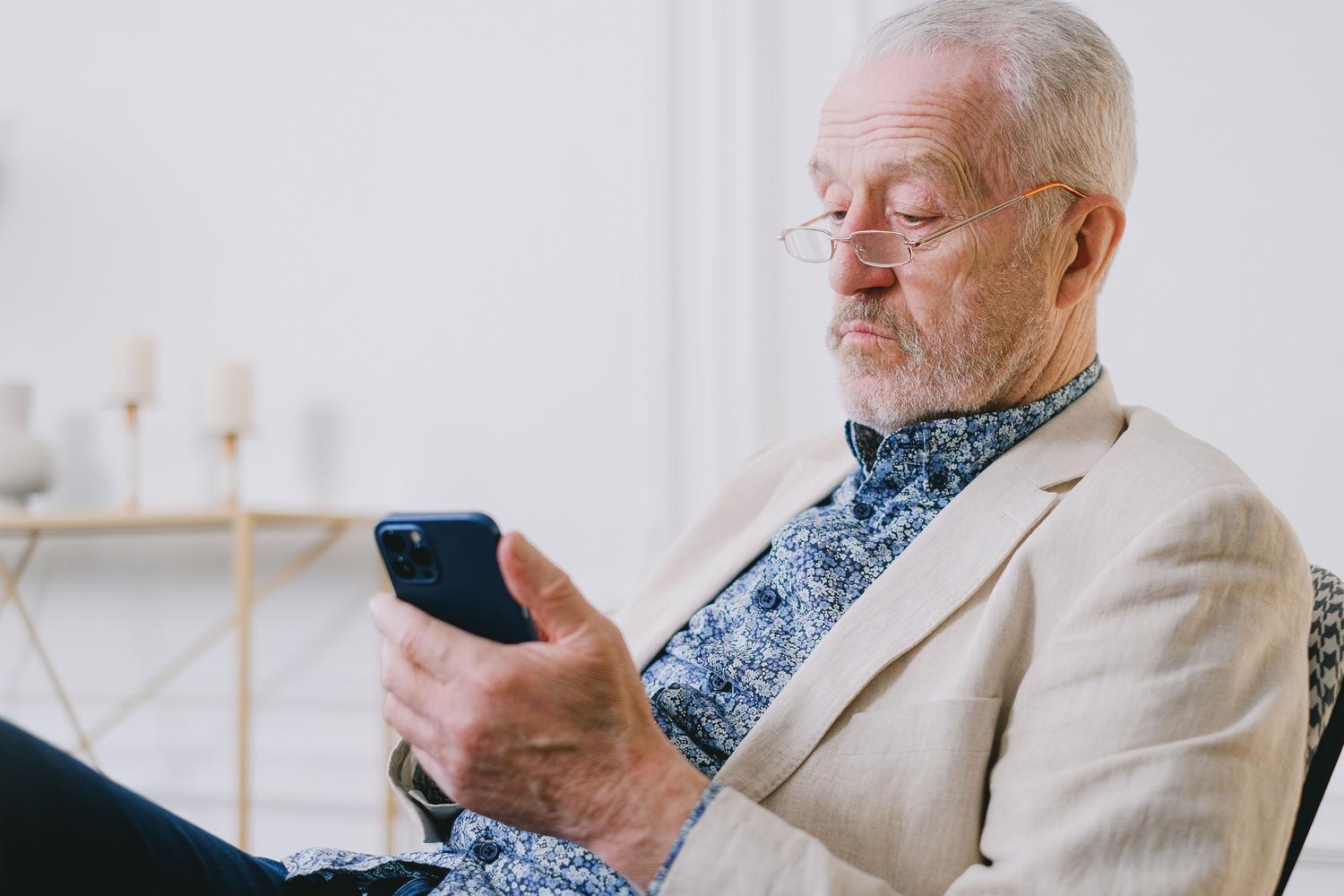 Tuvplāns vecākam vīrietim ar brillēm, izmantojot mobilo tālruni, ar mierīgu izteiksmi. Tuvplāns vecākam vīrietim ar brillēm, izmantojot mobilo tālruni, ar mierīgu izteiksmi.