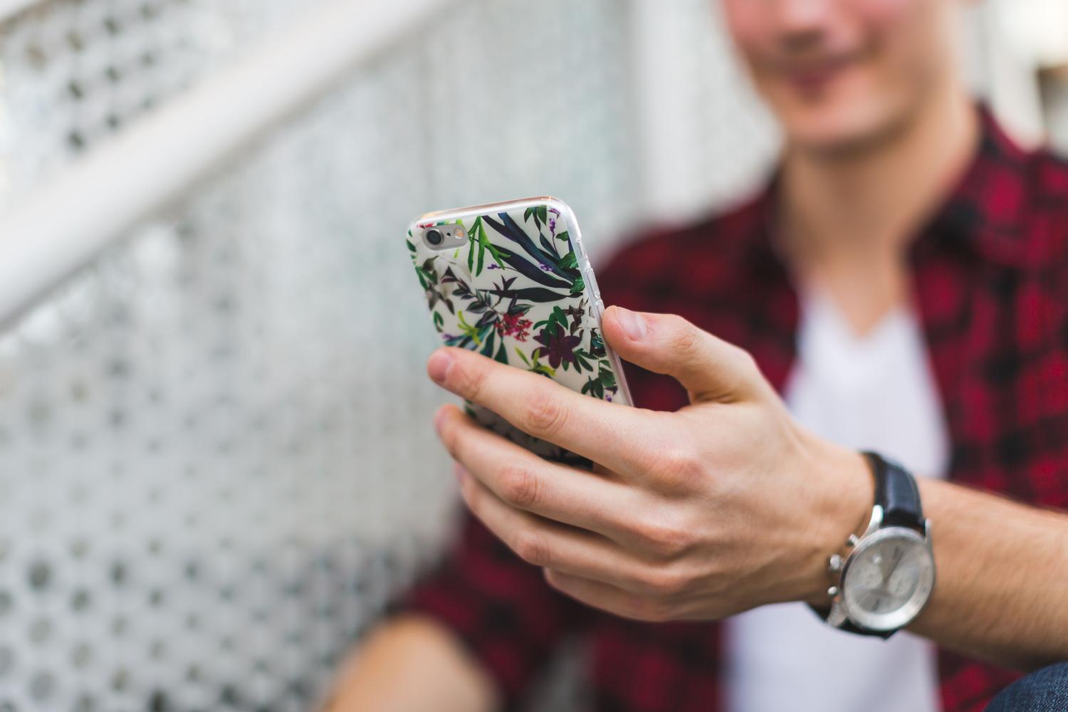 Koncentrēts cilvēks, kurš izmanto iPhone tālruni ar ziedu korpusu, kas izraisa personīgās dienasgrāmatas rakstīšanas intimitāti Koncentrēts cilvēks, kurš izmanto iPhone tālruni ar ziedu korpusu, kas izraisa personīgās dienasgrāmatas rakstīšanas intimitāti