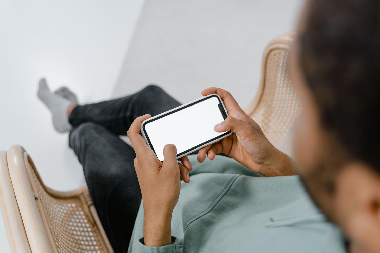 Skats no cilvēka pleca, kurš uzstāda iPhone tālruni ar neitrālu fonu